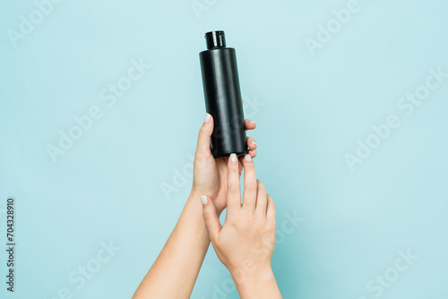 Hands hold black bottle of cosmetic product for skin on blue background photo