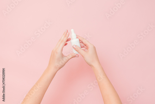 White bottle with serum lotion or essential oil (hyaluronic acid and collagen) in hands on pink background. Skin care cosmetics concept, beauty flyer