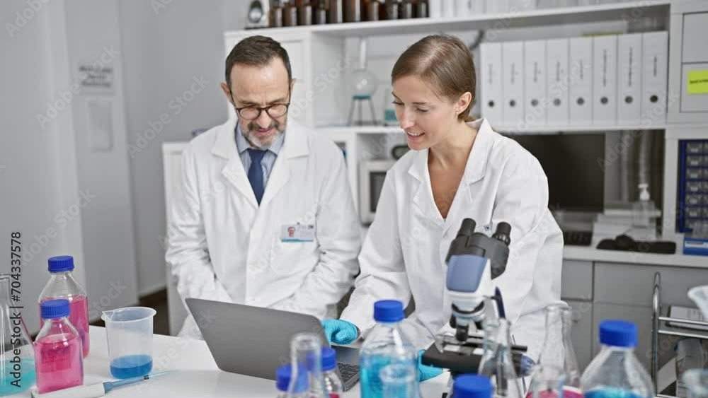 Two thrilled scientists high five at lab, celebrating discovery on laptop. man and woman, partners in science, beam amid a backdrop of test tubes and microscopes. Two thrilled scientists high five at lab, celebrating discovery on laptop. man and woman, partners in science, beam amid a backdrop of test tubes and microscopes.