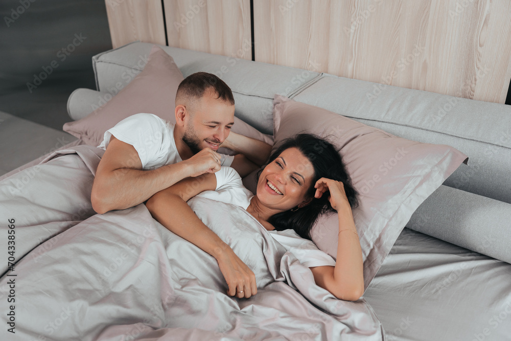 cheerful couple in casual wear lying in bed, sharing a joyful moment together in a modern bedroom with light decor cheerful couple in casual wear lying in bed, sharing a joyful moment together in a modern bedroom with light decor