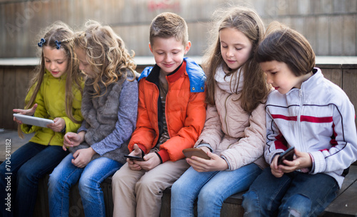 children playing in smartphones on street bench in park