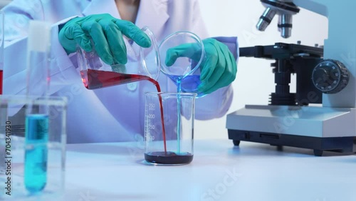 Asian people scientist in lab coat and protective gloves working with test tubes with mix liquids, with microscope and other test tubes in the background in laboratory.