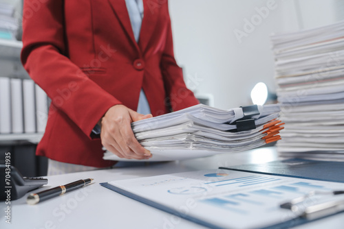 Wallpaper Mural stressed individual with glasses, wearing a red blazer, holding their head in one hand and a pen in the other, with a large stack of papers beside them. Torontodigital.ca