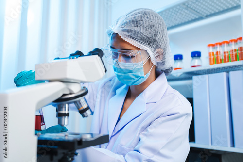 Asian people scientist in lab coat and protective gloves working with test tubes with green and red liquids, with microscope and other test tubes in the background in laboratory.