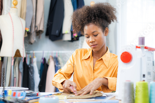 Young African American designer drawing on peice of fabric working in fashion studio room with intense emotion, Small business concept photo