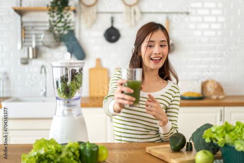 Portrait beauty healthy asian woman making green vegetables detox cleanse and green fruit smoothie with blender.young girl drinking glass of green fruit smoothie in kitchen.Diet concept.healthy drink