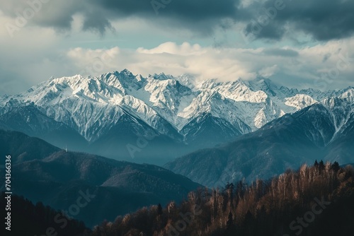 Coniferous forest against the backdrop of snow-capped mountains and cloudy skies. The concept for the development of tourism, mountaineering, skiing, rock climbing, excursions in the mountains.
