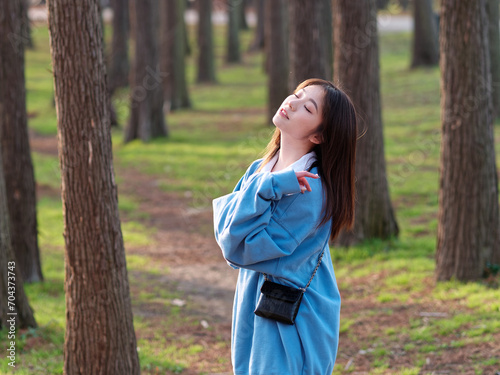 Beautiful young Chinese woman posing in sunny summer forest, wearing blue loose oversized top and miniskirt with small shoulder bag. Emotions, people, beauty, youth and lifestyle portrait.