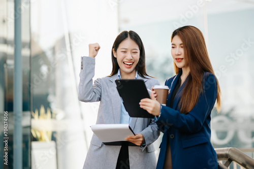 Businesswoman and woman going in city center in smart casual business style, talking, working together, stylish freelance people, holding tablet