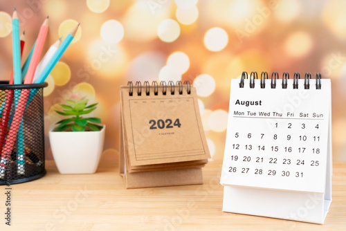White August 2024 desk calendar on wooden table with gold light bokeh background.