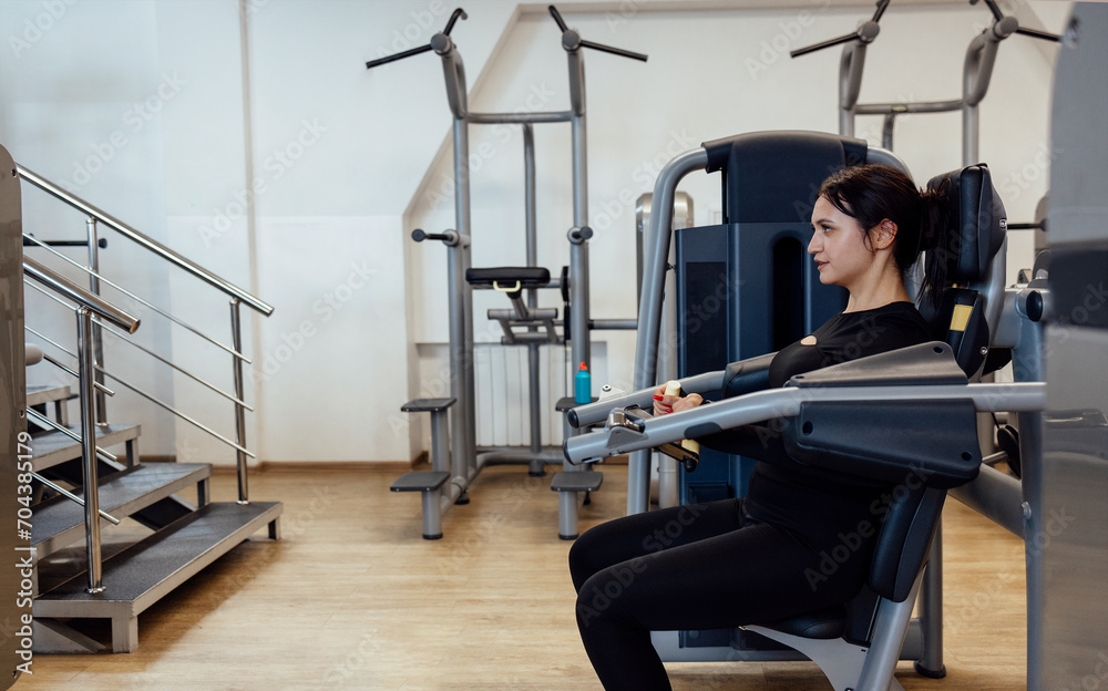 Obraz premium Attractive brunette sportive woman doing exercises on the simulator in fitness club