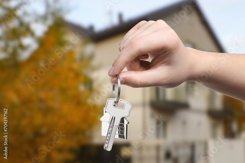 Woman holding key near house outdoors, closeup