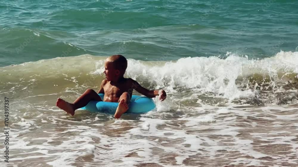 A happy child with a swimming circle swims on the sea on a sunny day. The boy has fun on the waves, moves his feet in the water, splashes, hitting the waves. Black Sea. 4K A happy child with a swimming circle swims on the sea on a sunny day. The boy has fun on the waves, moves his feet in the water, splashes, hitting the waves. Black Sea. 4K