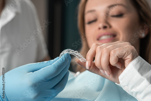 Attentive dentist demonstrating aligner aligner in hands, showing female patient in dental office, preparing for work and striving to make the procedure as comfortable as possible for her patient.