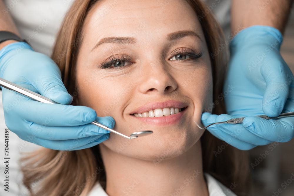 The dentist, holding the instruments, confidently and carefully treats the patient, providing a painless and professional approach. Woman smiling with white teeth charming smile close-up