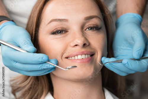 The dentist, holding the instruments, confidently and carefully treats the patient, providing a painless and professional approach. Woman smiling with white teeth charming smile close-up