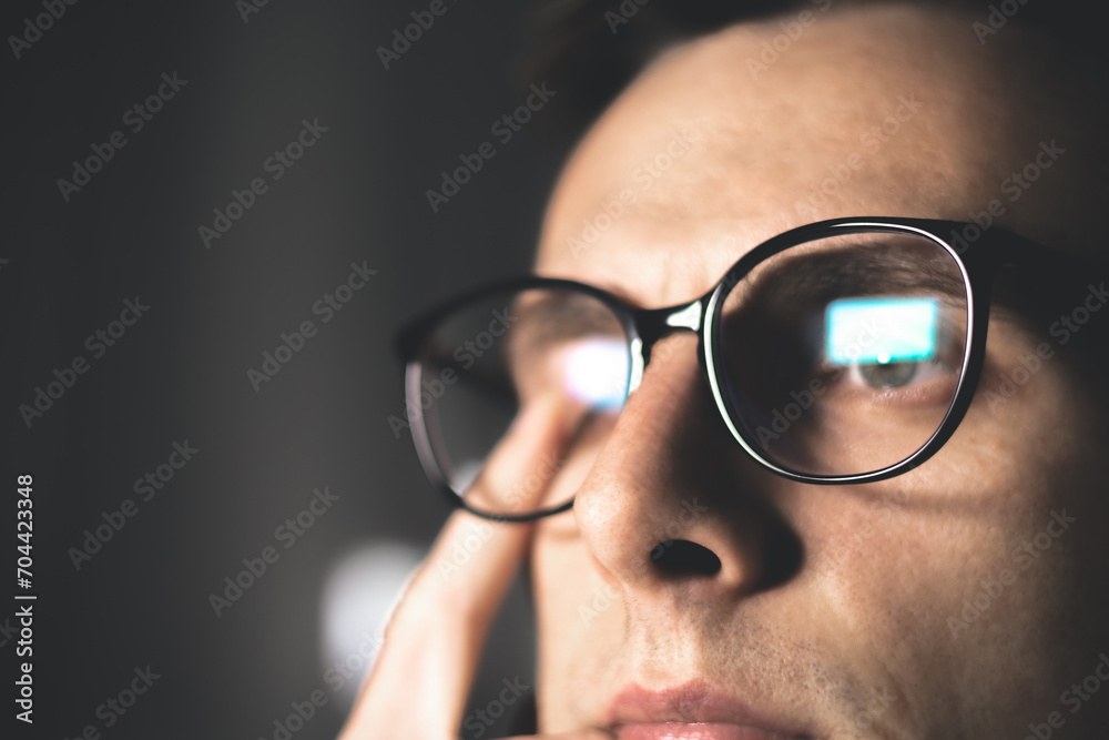 Tired man in glasses works on internet. Migraine or headache after work in front of computer all day. Eye pain, dry eye syndrome. Tired man in glasses works on internet. Migraine or headache after work in front of computer all day. Eye pain, dry eye syndrome.