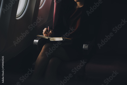Blonde female tourist checking incoming notification on smartphone sitting on seat of airplane with netbook.Young businesswoman share media from telephone on laptop computer during plane flight