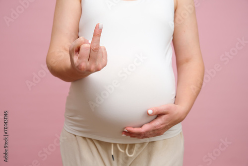 Pregnant woman showing middle finger gesture with hand, studio pink background photo