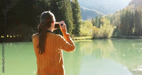 Young woman at a scenic alpine lake in Jezersko, Slovenia. Female photographer with camera. Handheld footage on a sunny autumn day in the Alps. photo