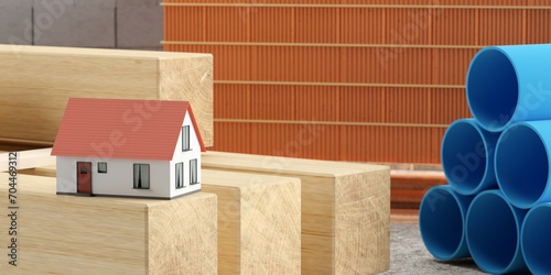 Fototapeta Naklejka Na Ścianę i Meble -  Miniature house model on wood beams in front of collection of building or construction materials with concrete bricks and pvc pipes, selective focus