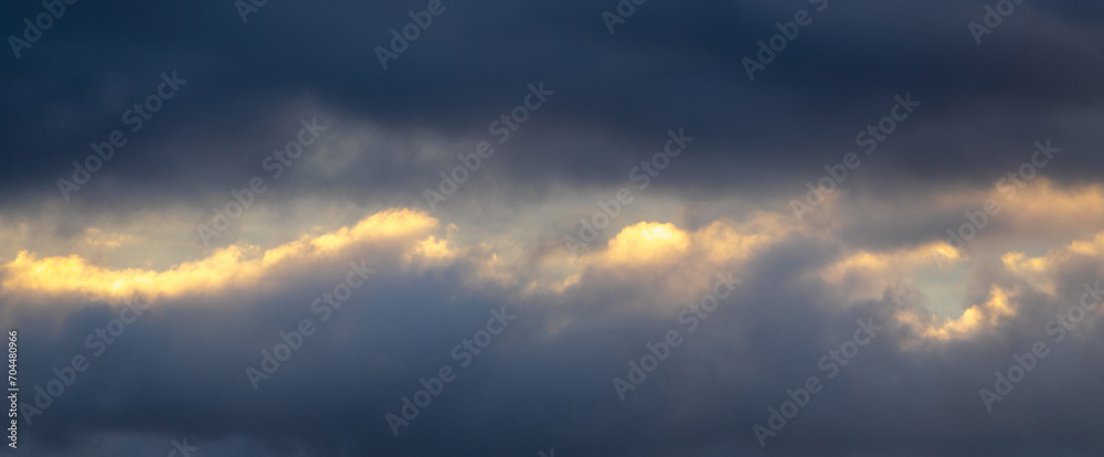 A patch of sky illuminated by the evening sun shines through the dark blue clouds