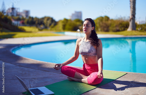 Hispanic woman meditating next to a pool outdoors