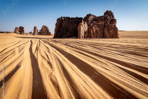 Landscape of Erg Admer in the Sahara desert, Algeria. The tracks of numerous jeeps converge towards the rock formations of the La Vache Qui Pleure site. photo