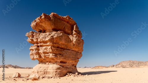 Tadrart landscape in the Sahara desert, Algeria. A block of sandstone stands alone on the sand