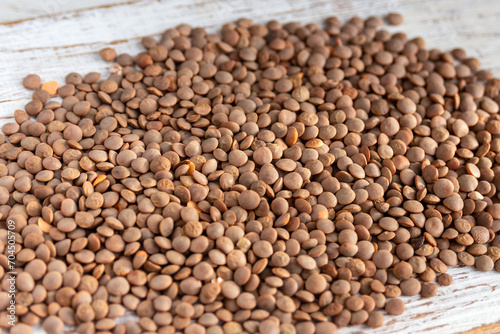 Scattered wild raw organic lentils on a white wooden board.