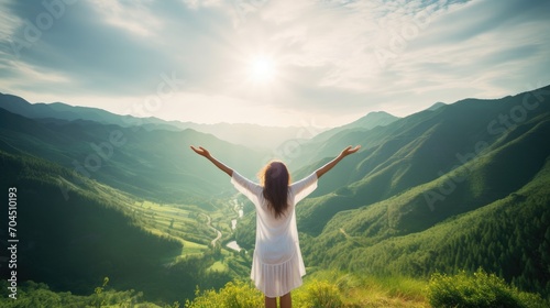 Beautiful happy girl in a light dress opens her arms towards the sun on the background of blue sky and green mountains in the summer morning 