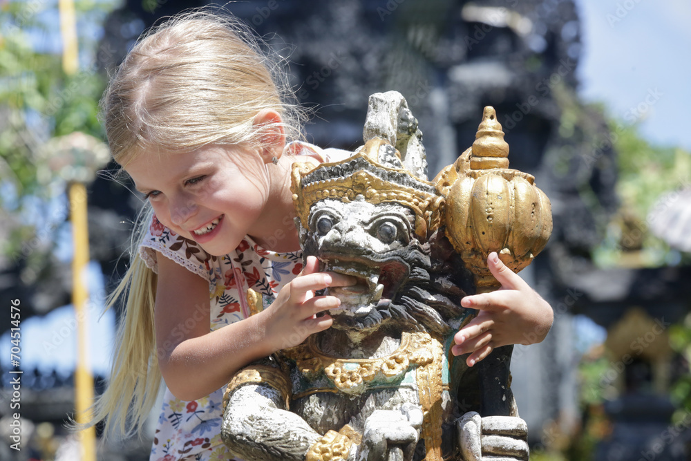 Naklejka premium Outdoor portrait of young girl with traditional Balinese statue of Barong on a street temple in Bali, Indonesia