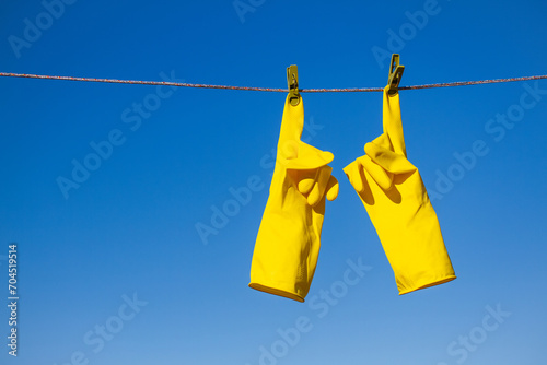 Obraz na plátne Yellow rubber protective gloves for work or cleaning hanging on a rope with a clothespin against a blue sky background