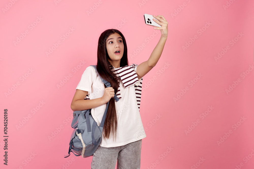 Young shocked teenage girl taking a selfie with phone with bag on pink background in studio. Young shocked teenage girl taking a selfie with phone with bag on pink background in studio.