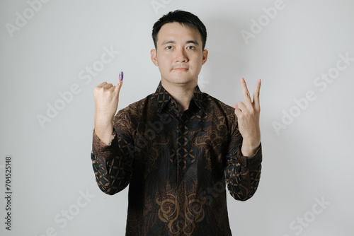 Asian man wearing Indonesian traditional Batik cloth is showing his little finger with purple ink applied to choose number two after Pemilu or Indonesian presidential election on white background photo