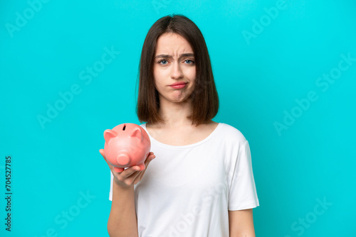 Young Ukrainian woman holding a piggybank isolated on blue background with sad expression