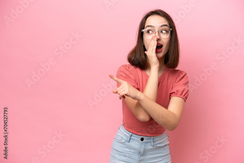 Young Ukrainian woman isolated on pink background pointing to the side to present a product and whispering something