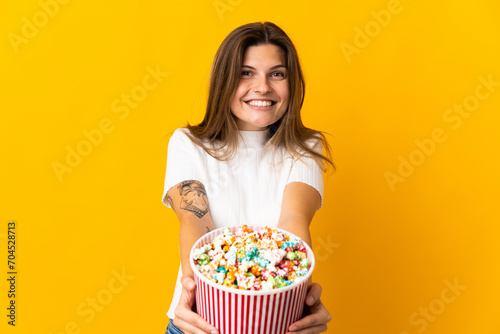 Young slovak woman isolated on yellow background holding a big bucket of popcorns