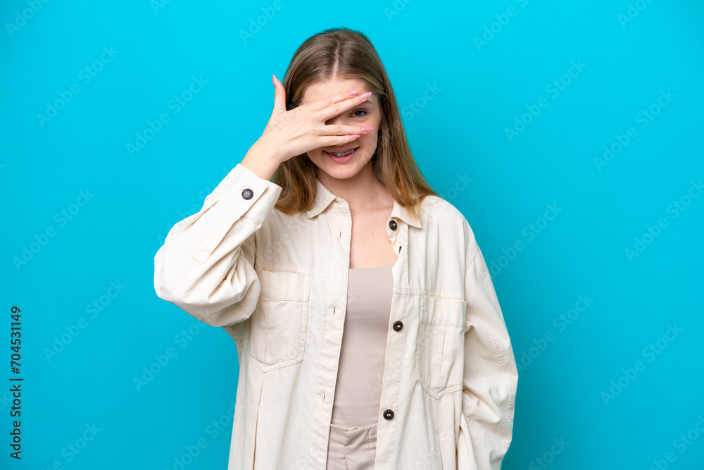 Teenager Russian girl isolated on blue background covering eyes by hands and smiling Teenager Russian girl isolated on blue background covering eyes by hands and smiling