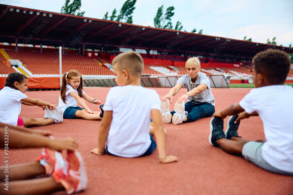 Fototapeta premium Group of kids and their sports teacher warming up at stadium.
