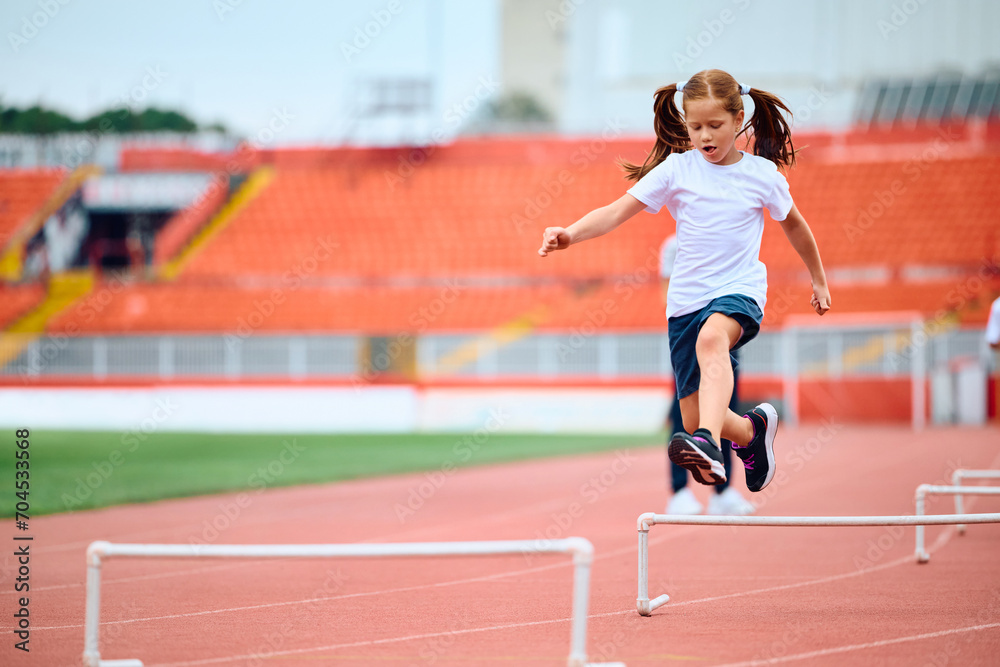 Small girl hurdling on sports training at athletics club.