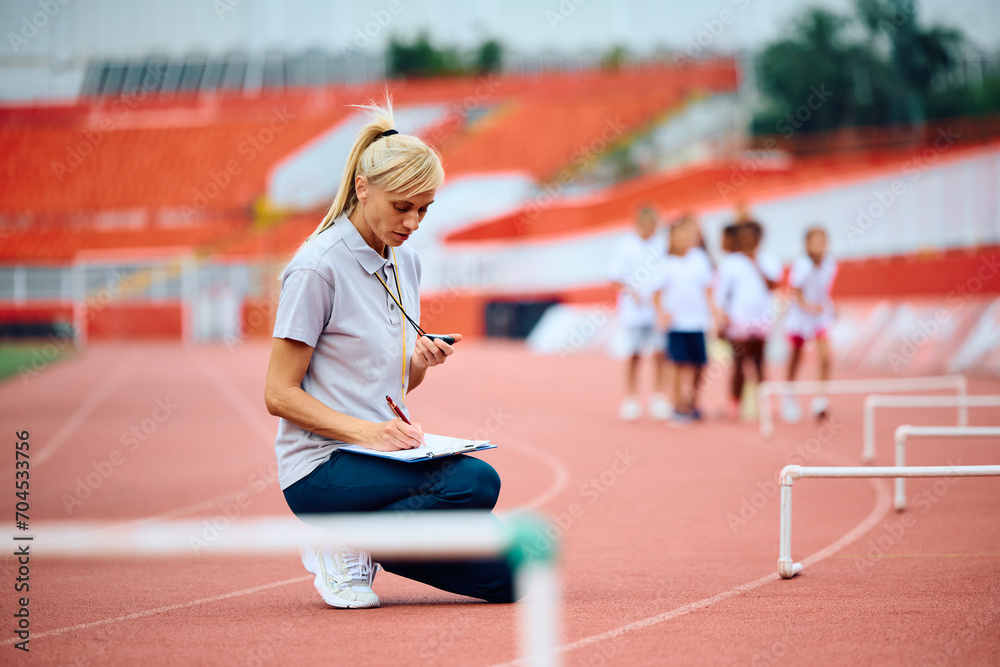 Athletics coach writing on clipboard during sports training at stadium.