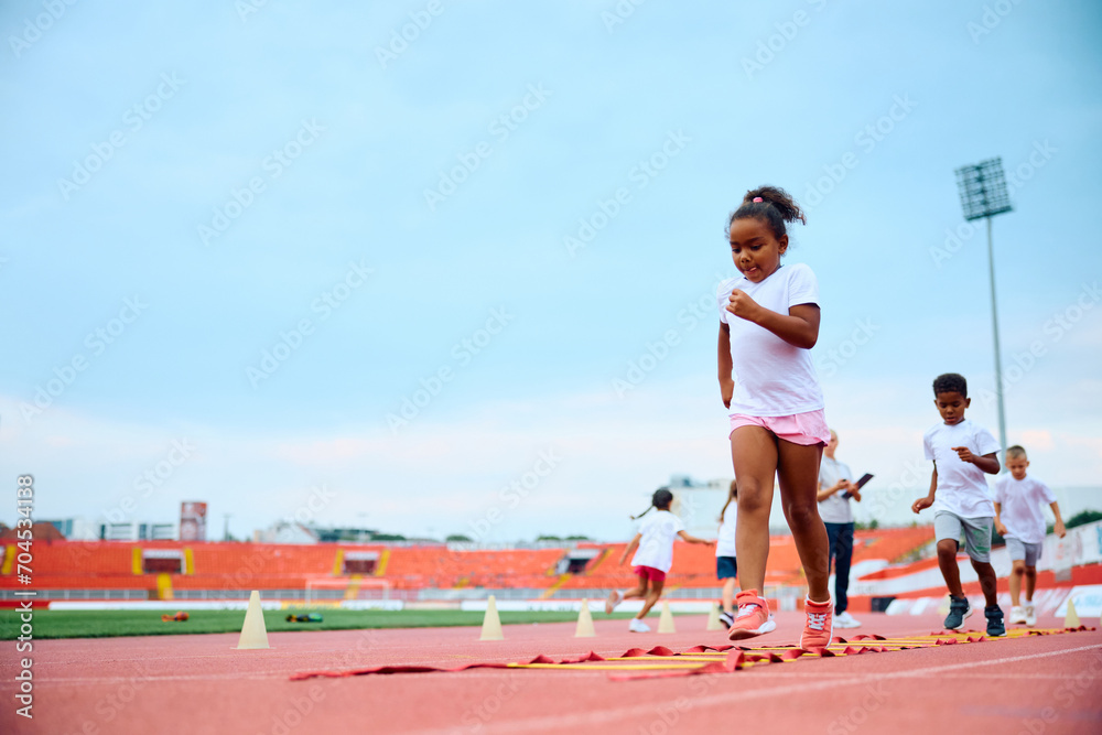 Black little girl and her friends having exercise class at stadium.