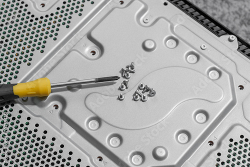 Screwdriver and small screws on perforated metal cover. Electronic components disassembly for upgrade