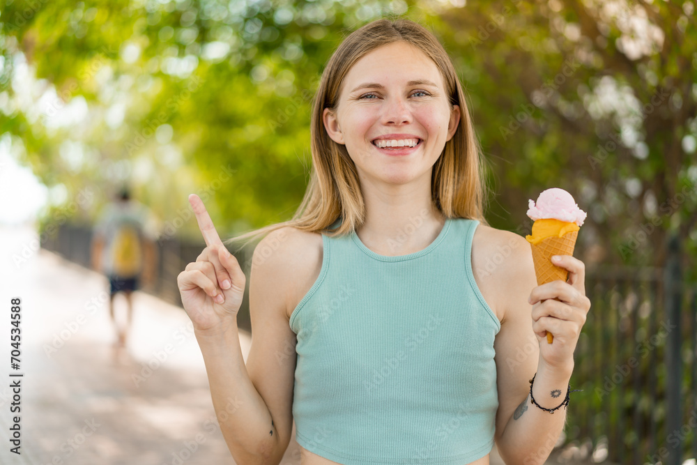 Young blonde pretty woman with a cornet ice cream at outdoors pointing up a great idea Young blonde pretty woman with a cornet ice cream at outdoors pointing up a great idea