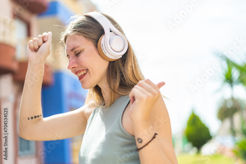 Young blonde woman at outdoors listening music and dancing