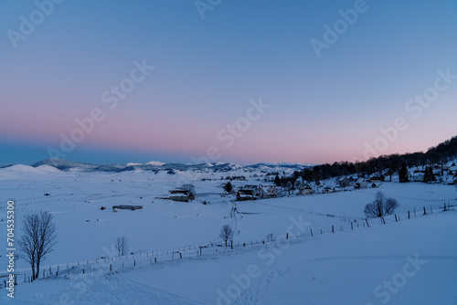 Pink-blue sunset over a snow-covered village on the edge of a forest in a mountain valley