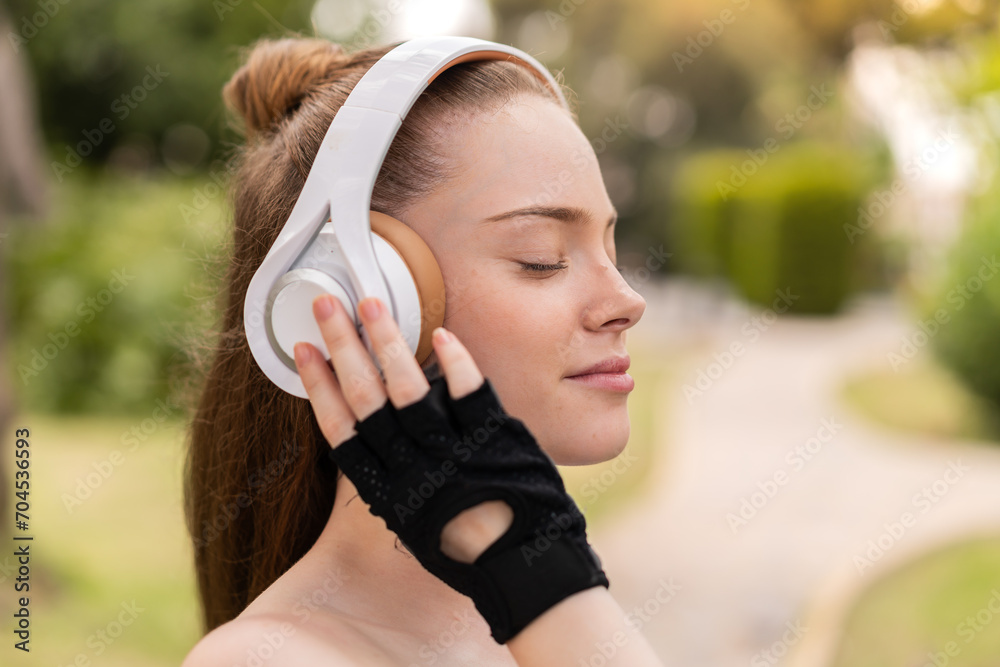 Young pretty girl at outdoors wearing sport wear and listening music with headphones - obrazy, fototapety, plakaty 