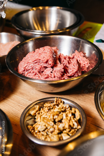 Ground Beef and Walnuts in Stainless Steel Bowls. Raw ground beef ready for cooking and a bowl of walnuts presented as ingredients on a warm wooden kitchen surface.