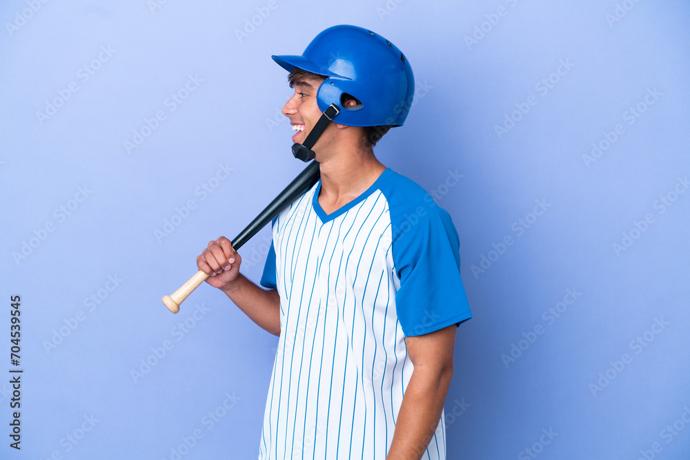 Baseball caucasian man player with helmet and bat isolated on blue background laughing in lateral position Baseball caucasian man player with helmet and bat isolated on blue background laughing in lateral position